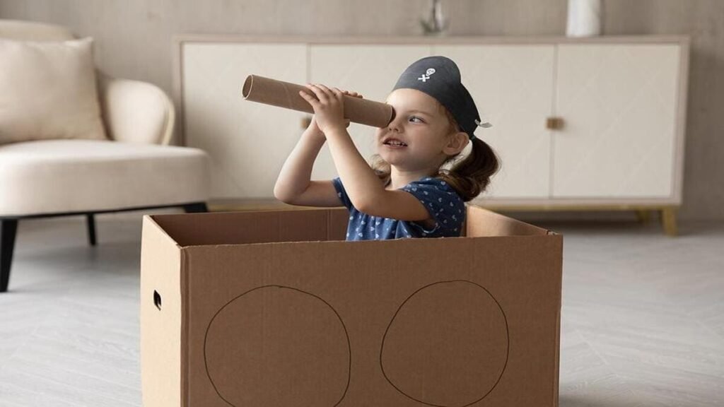 A young girl sitting inside a cardboard box pretending to be a pirate