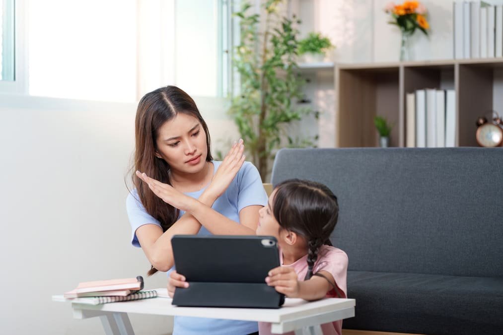 Mum in scrubs calmly ending screen time with young child at home in the evening