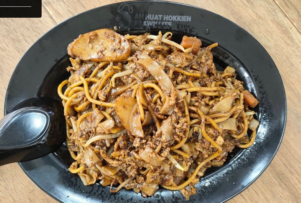 Plate of char kway teow from a Singapore kopitiam — flat rice noodles, cockles, and egg