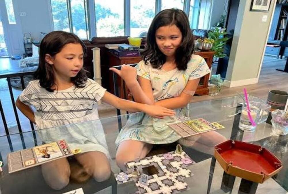 Two children rolling dice and exploring the tile dungeon while playing the board game Karak at a table