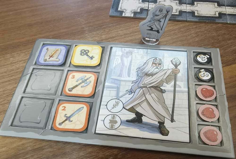 A Karak character board showing a hero with two equipment slots filled, alongside health tokens and treasure